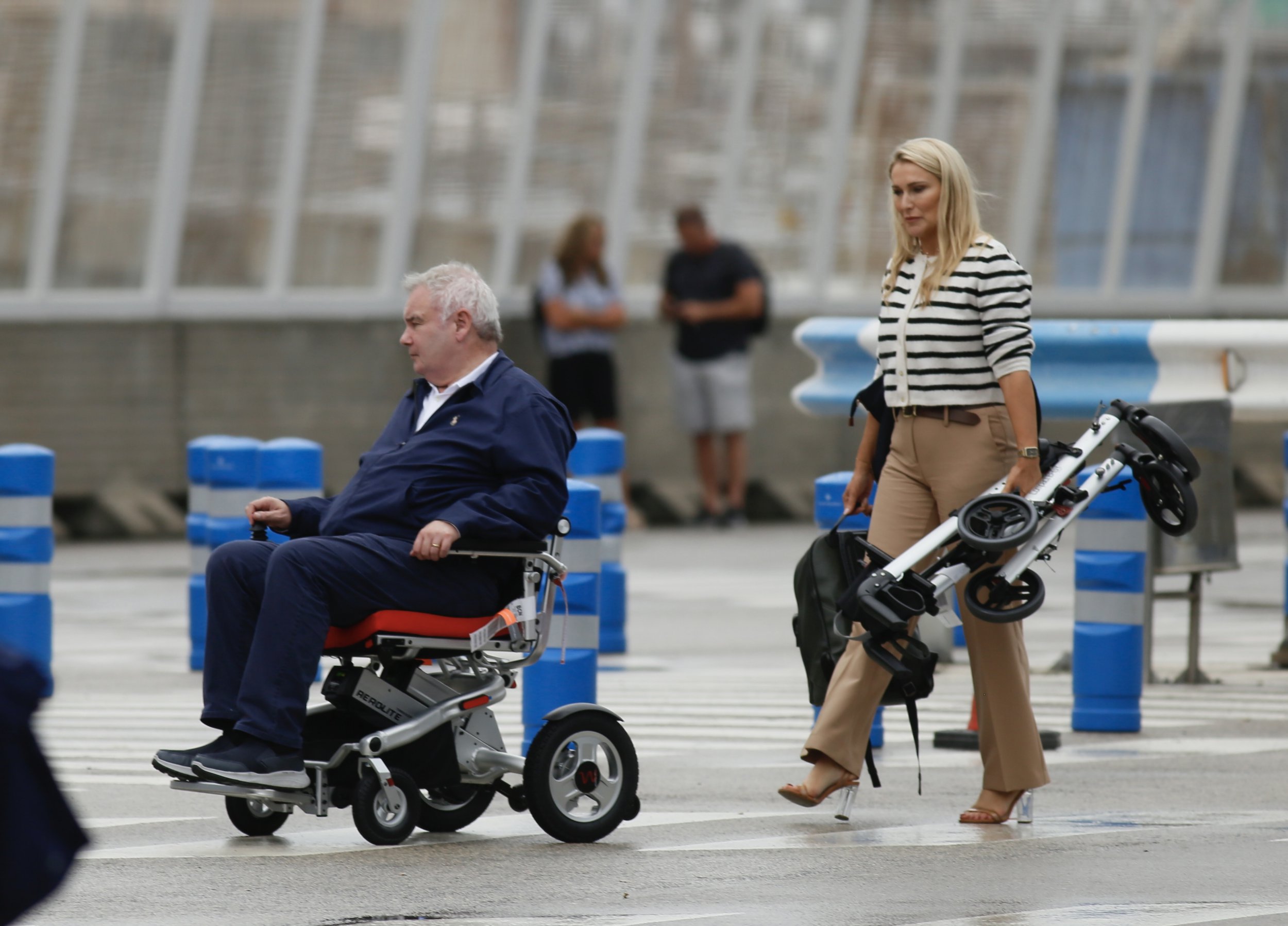 Eamonn Holmes using a wheelchair followed by Katie Alexander holding his walker
